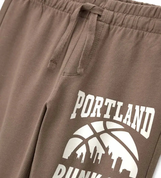 Λεπτομέρεια από το λάστιχο και το διακοσμητικό τύπωμα στο παιδικό καφέ παντελόνι.