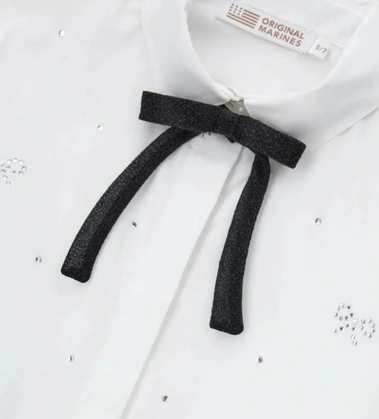 Παιδικό πουκάμισο από βαμβάκι με κουμπιά στο μπροστινό μέρος, μακριά μανίκια και μανσέτες με κουμπί. Διαθέτει αφαιρούμενο φιόγκο από λαμιναρισμένο ύφασμα και στρας στο μπροστινό μέρος και στα μανίκια για ένα λαμπερό και μοντέρνο στυλ.