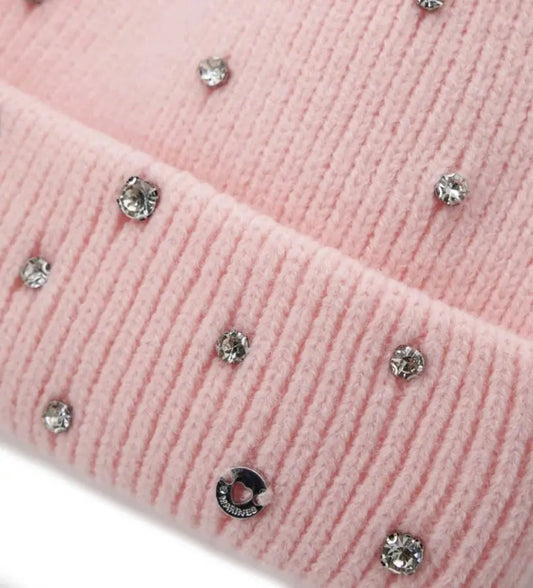 Πλεκτό σκουφάκι με ρεβέρ, διακοσμημένο με στρας για λαμπερή εμφάνιση. Ένα αξεσουάρ που συνδυάζει άνεση και στυλ, ιδανικό για να προσθέσει μια πινελιά φωτός και κομψότητας στις χειμερινές εμφανίσεις.