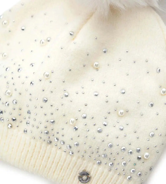 Πλεκτό σκουφάκι διακοσμημένο με στρας, τρουκς και πέρλες, ολοκληρωμένο με φουντάκι από οικολογική γούνα. Ένα ζεστό και κομψό αξεσουάρ που συνδυάζει στυλ και άνεση, χαρίζοντας μια πινελιά κλάσης στις χειμερινές εμφανίσεις.