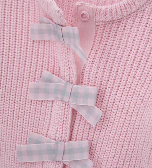 Παιδική ζακέτα από βαμβακερό νήμα με στρογγυλή λαιμόκοψη, ριμπ τελειώματα και μακριά μανίκια. Διαθέτει μπροστινό άνοιγμα με κρυφά κουμπιά-σούστες, διακοσμητικούς φιόγκους από καρό ύφασμα και μενταγιόν στο μπροστινό μέρος. Ένα εκλεπτυσμένο και απαλό κομμάτι, ιδανικό για κοριτσίστικες εμφανίσεις με ρομαντικό στυλ.