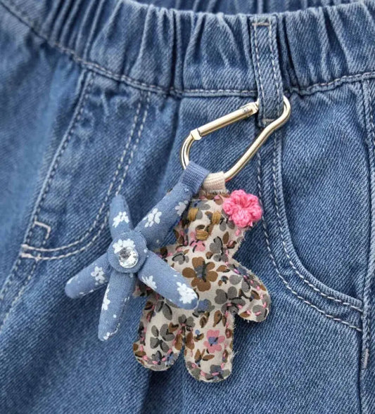 Κοντινό πλάνο στα διακοσμητικά charms (αρκουδάκι και λουλούδι) που κρέμονται από το τζιν παντελόνι.