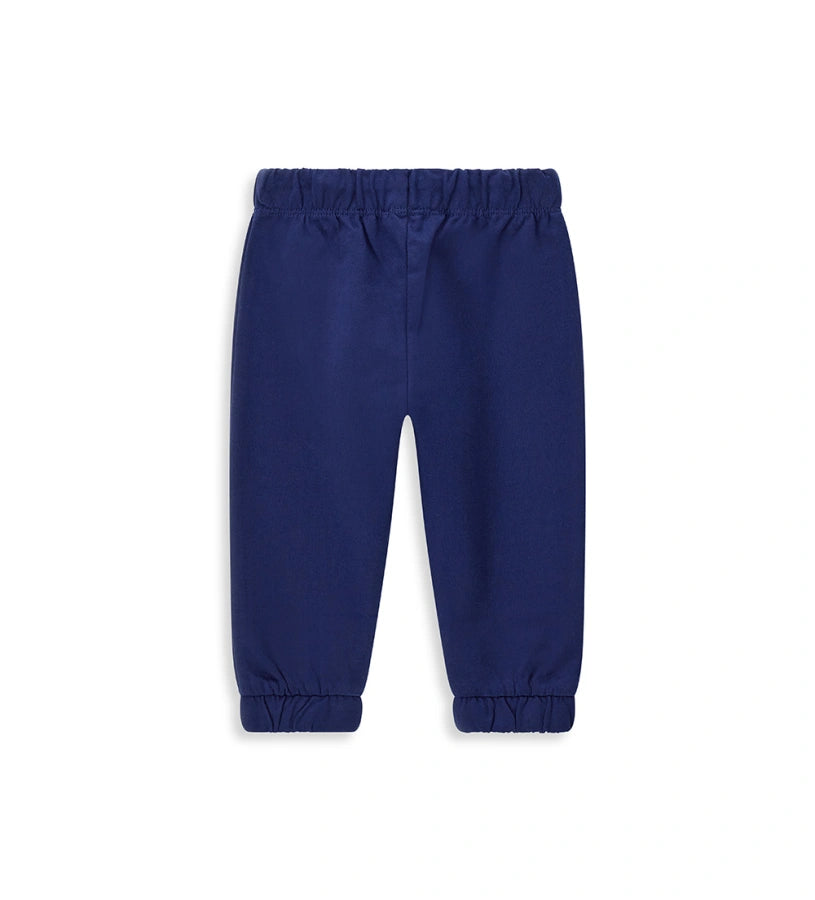 Παιδικό παντελόνι σε μπλε χρώμα από ελαστικό βαμβακερό fleece, ιδανικό για καθημερινή άνεση. Διαθέτει ρυθμιζόμενη μέση με κορδόνι και διακριτικό τύπωμα στο μπροστινό μέρος. Ένα πρακτικό και μοντέρνο κομμάτι για κάθε παιδική εμφάνιση.