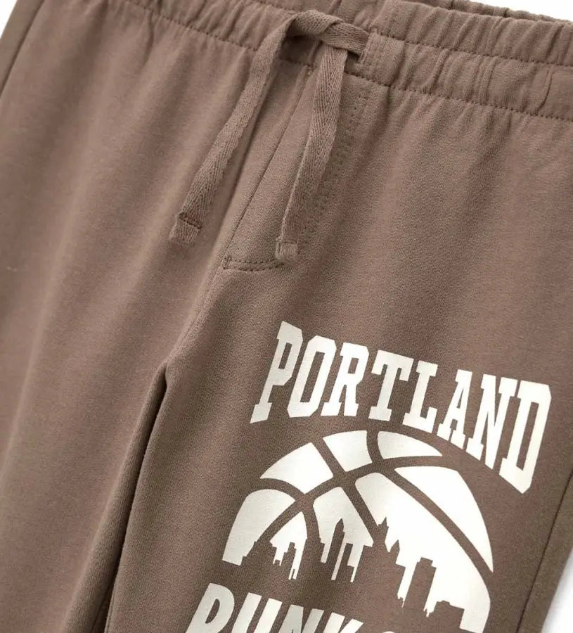 Λεπτομέρεια από το λάστιχο και το διακοσμητικό τύπωμα στο παιδικό καφέ παντελόνι.