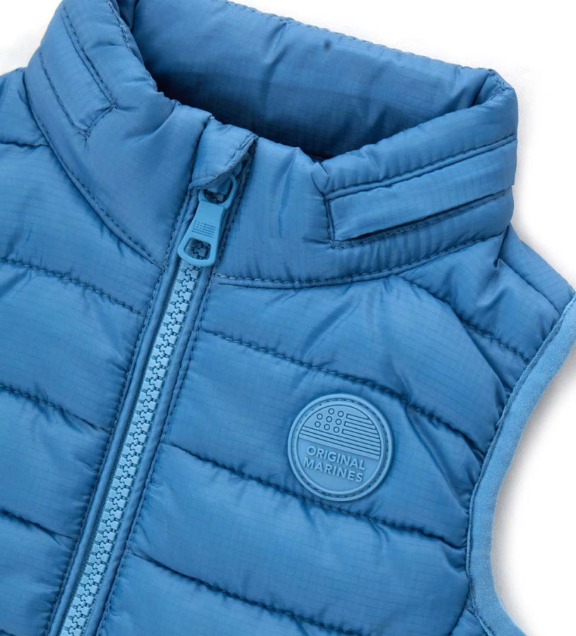 Παιδικό καπιτονέ γιλέκο από ανθεκτικό ripstop νάιλον με αποσπώμενη κουκούλα για μεγαλύτερη ευελιξία. Διαθέτει άνοιγμα με φερμουάρ, τσέπες με φερμουάρ και ελαστικά τελειώματα για άνετη εφαρμογή. Ιδανικό για layering τις πιο δροσερές μέρες, συνδυάζει πρακτικότητα και στυλ σε κάθε εμφάνιση.