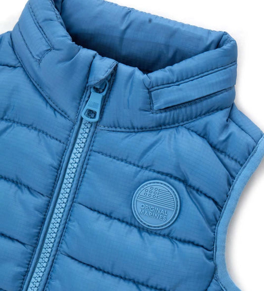 Παιδικό καπιτονέ γιλέκο από ανθεκτικό ripstop νάιλον με αποσπώμενη κουκούλα για μεγαλύτερη ευελιξία. Διαθέτει άνοιγμα με φερμουάρ, τσέπες με φερμουάρ και ελαστικά τελειώματα για άνετη εφαρμογή. Ιδανικό για layering τις πιο δροσερές μέρες, συνδυάζει πρακτικότητα και στυλ σε κάθε εμφάνιση.