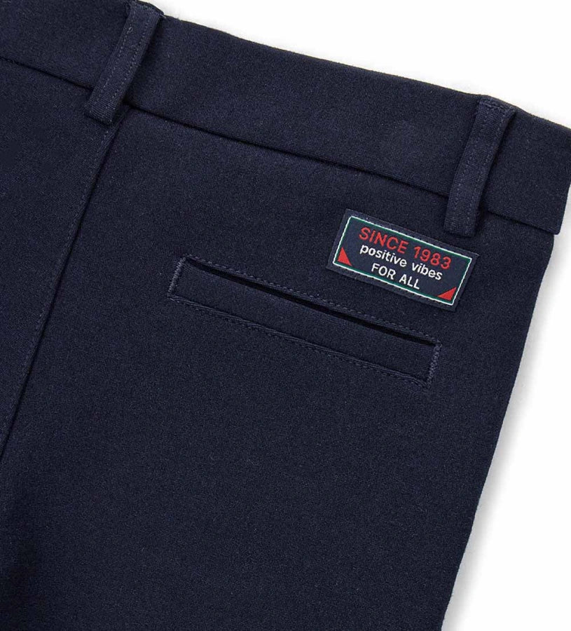 Παντελόνι chinos από ύφασμα Milano. Διαθέτει ρυθμιζόμενη μέση, πρακτικές τσέπες και κομψή κεντημένη ετικέτα στο πίσω μέρος. Για τα μεγέθη έως 2–3 ετών το άνοιγμα είναι με κουμπί, ενώ από το μέγεθος 3–4 ετών και πάνω διαθέτει φερμουάρ.