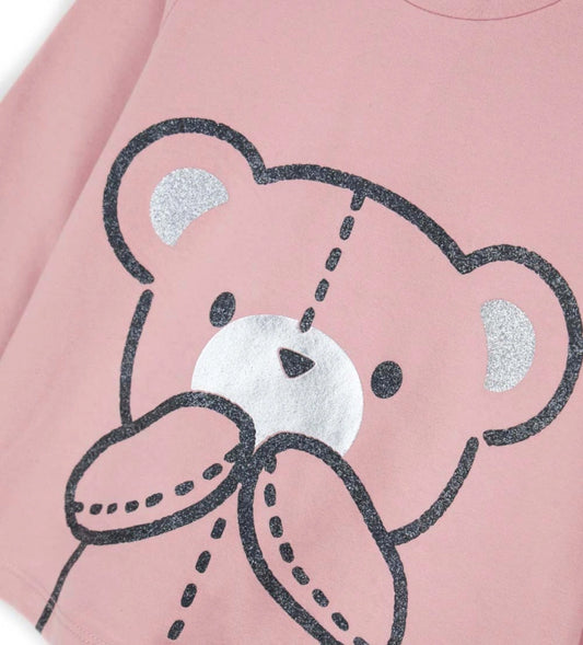 Μπλούζα από ελαστικό βαμβάκι με στρογγυλή λαιμόκοψη, μακριά μανίκια, βολάν στους ώμους και τύπωμα με γκλίτερ και μεταλλικές λεπτομέρειες στο μπροστινό μέρος. Για τα μεγέθη έως 2–3 ετών διαθέτει πρακτικό άνοιγμα με κουμπιά.