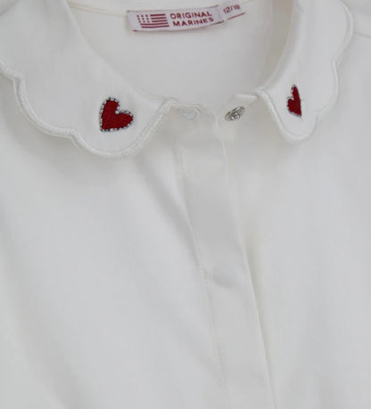 Παιδικό κορμάκι-πουκάμισο από βαμβακερό ποπλίνα με κόψιμο στη μέση και κάτω μέρος από βαμβακερό jersey για άνετη εφαρμογή. Διαθέτει γιακά με κέντημα καρδιάς, μπροστινό άνοιγμα με κουμπιά και κουμπιά στο εσωτερικό του καβάλου και στις μανσέτες. Ένα κομψό και πρακτικό κομμάτι, ιδανικό για ιδιαίτερες εμφανίσεις με στυλ.