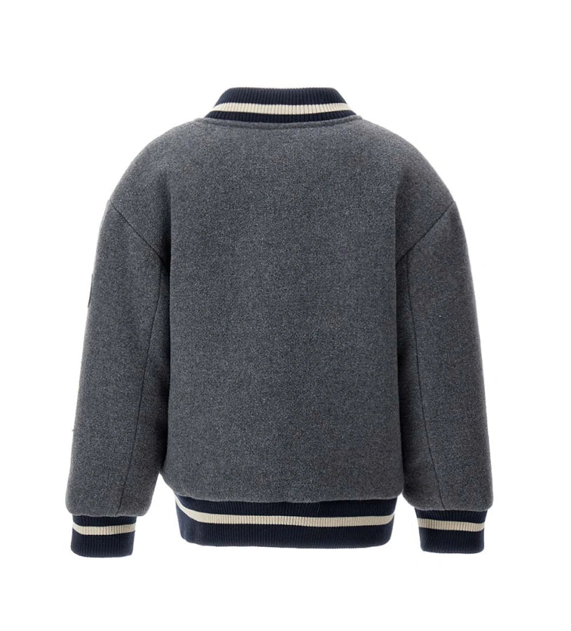 Παιδικό μπουφάν bomber από ύφασμα τύπου μάλλινο με μπροστινές τσέπες και καπιτονέ, επενδυμένη εσωτερική φόδρα για επιπλέον άνεση. Διαθέτει άνοιγμα με κουμπιά-σούστες και ριμπ τελειώματα σε χρώμα βαφής. Ένα ζεστό και μοντέρνο κομμάτι, ιδανικό για στιλάτες χειμερινές εμφανίσεις.