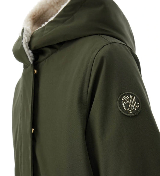 Μακρύ παρκά με κουκούλα και αποσπώμενη επένδυση από οικολογική γούνα μέσω κρυφών φερμουάρ. Κλείσιμο με φερμουάρ και κουμπιά σούστες, μπροστινές τσέπες και διακοσμημένο έμβλημα με στρας. Ένα πρακτικό και ταυτόχρονα λαμπερό ρούχο, ιδανικό για κομψές και ζεστές χειμερινές εμφανίσεις.