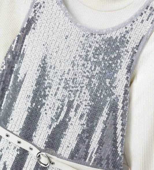 Σετ που αποτελείται από αμάνικο φόρεμα από ύφασμα με παγιέτες, με εσωτερική φόδρα, στρογγυλή λαιμόκοψη και άνοιγμα στο πίσω μέρος, καθώς και ζιβάγκο τοπ με μακριά ριπ μανίκια, για κομψή και λαμπερή εμφάνιση.