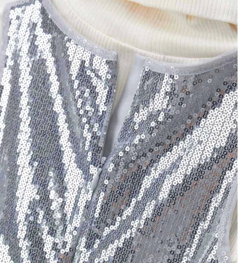 Σετ που αποτελείται από αμάνικο φόρεμα από ύφασμα με παγιέτες, με εσωτερική φόδρα, στρογγυλή λαιμόκοψη και άνοιγμα στο πίσω μέρος, καθώς και ζιβάγκο τοπ με μακριά ριπ μανίκια, για κομψή και λαμπερή εμφάνιση.