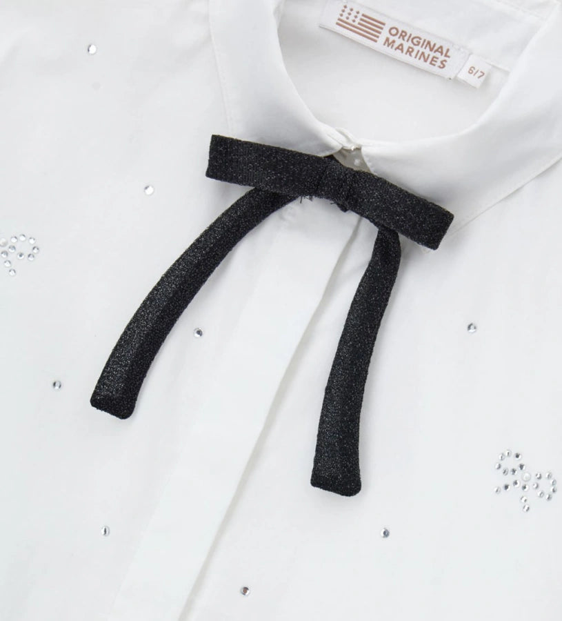 Παιδικό πουκάμισο από βαμβάκι με κουμπιά στο μπροστινό μέρος, μακριά μανίκια και μανσέτες με κουμπί. Διαθέτει αφαιρούμενο φιόγκο από λαμιναρισμένο ύφασμα και στρας στο μπροστινό μέρος και στα μανίκια για ένα λαμπερό και μοντέρνο στυλ.