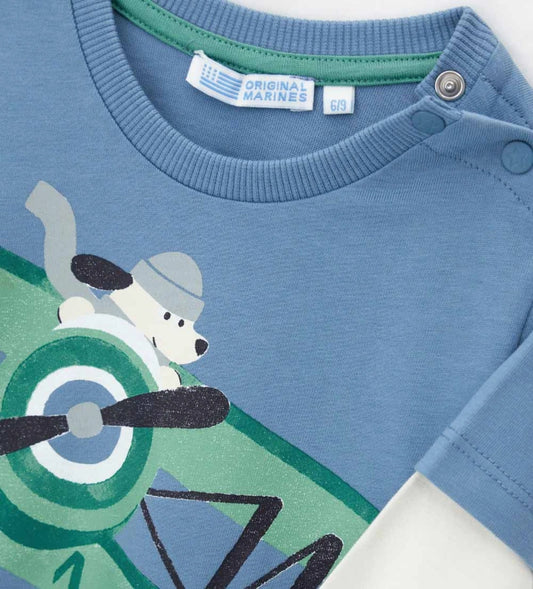 Βρεφική μπλούζα από βαμβάκι με διπλό μανίκι σε μπλε αντίθεση, στρογγυλή λαιμόκοψη με ριμπ τελείωμα και πρακτικό άνοιγμα στον ώμο με κουμπιά-σούστες. Διακοσμημένη με τύπωμα στο μπροστινό μέρος, προσφέρει άνεση και μοντέρνο στυλ για κάθε μέρα.