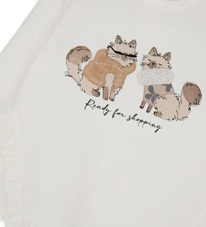 Βαμβακερή μπλούζα με στρογγυλή λαιμόκοψη και μακριά μανίκια. Διαθέτει πρακτικό άνοιγμα με κουμπιά-σούστες στο πίσω μέρος και είναι διακοσμημένη με βολάν, τύπωμα και κέντημα στο μπροστινό μέρος, για μοντέρνα και απαλή εμφάνιση.