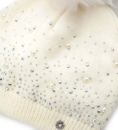 Πλεκτό σκουφάκι διακοσμημένο με στρας, τρουκς και πέρλες, ολοκληρωμένο με φουντάκι από οικολογική γούνα. Ένα ζεστό και κομψό αξεσουάρ που συνδυάζει στυλ και άνεση, χαρίζοντας μια πινελιά κλάσης στις χειμερινές εμφανίσεις.