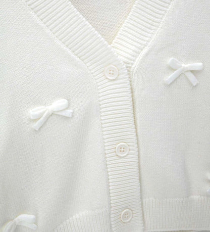 Πλεκτή ζακέτα από μείγμα μαλλιού με εμπρός άνοιγμα με κουμπιά και ριμπ τελειώματα σε λαιμό και μανσέτες. Διακοσμημένη με φιόγκους από μείγμα μαλλιού και μεταλλικό μενταγιόν για μια κομψή και εκλεπτυσμένη εμφάνιση.