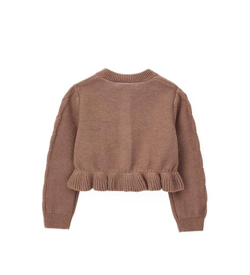 Παιδική ζακέτα από βαμβακερό νήμα με στρογγυλή λαιμόκοψη, ριμπ τελειώματα και μακριά μανίκια. Διαθέτει μπροστινό άνοιγμα με κουμπιά, πλέξη σε σχέδιο πλεξούδας, διακοσμητικό βολάν στο κάτω μέρος και μενταγιόν στο μπροστινό μέρος. Ιδανική για κομψές και απαλές κοριτσίστικες εμφανίσεις με ρομαντικό ύφος.