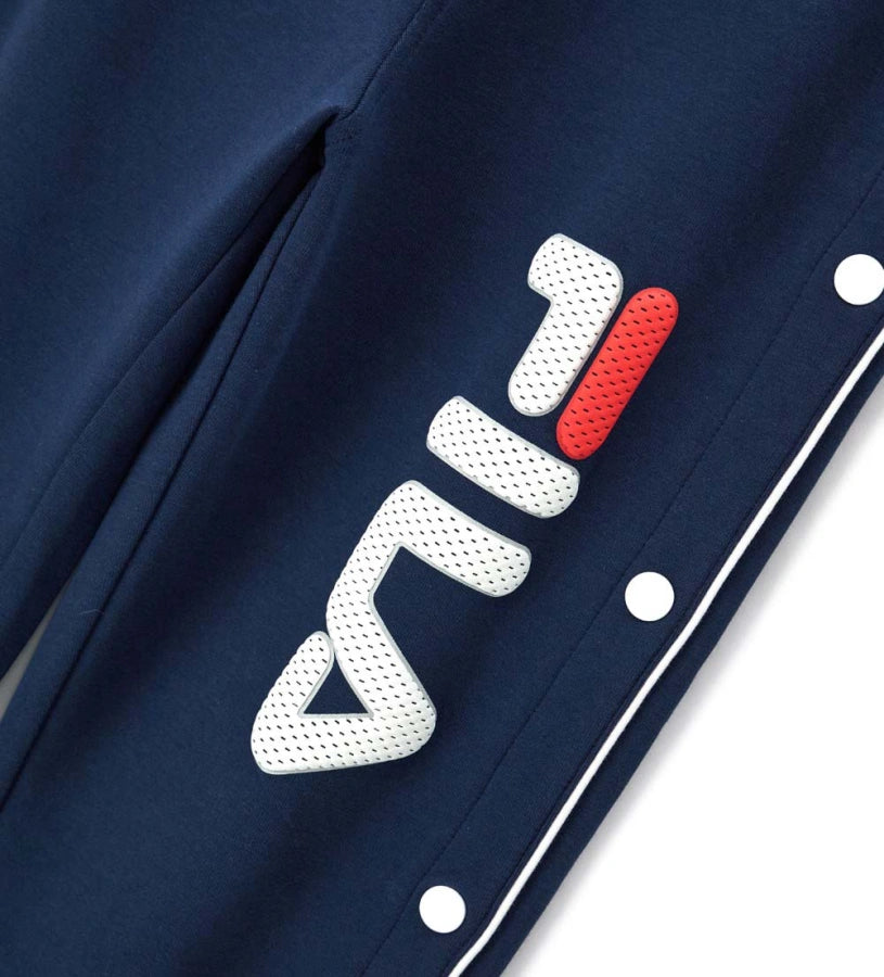 Παιδικό παντελόνι Fila από τεχνικό ύφασμα με ρυθμιζόμενο κορδόνι στη μέση και κουμπιά-σούστες στο κάτω μέρος. Διαθέτει τυπωμένο λογότυπο στο μπροστινό μέρος και διακοσμητική εφαρμογή στο πίσω, προσφέροντας αθλητικό και μοντέρνο στυλ για κάθε casual εμφάνιση.