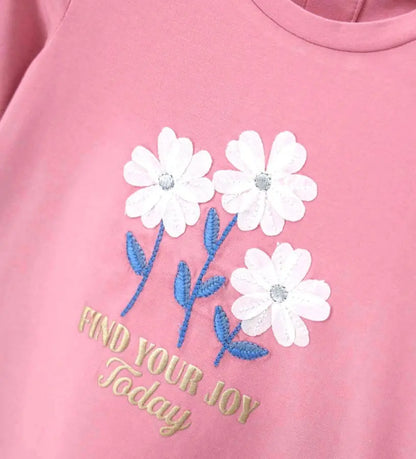 Κοντινό πλάνο στα λουλούδια crepe και τις μεταλλικές λεπτομέρειες της παιδικής μπλούζας.