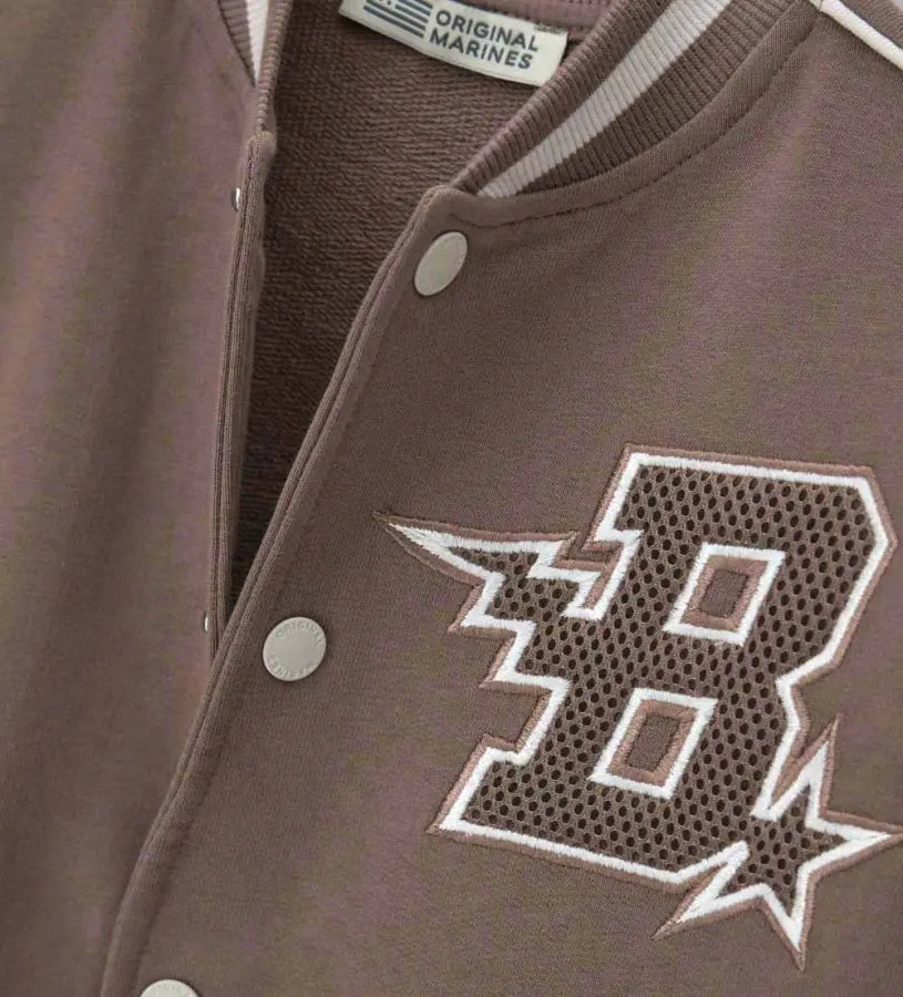 Λεπτομέρεια από το κεντημένο απλικέ και τα κουμπιά σούστες στο παιδικό varsity jacket.